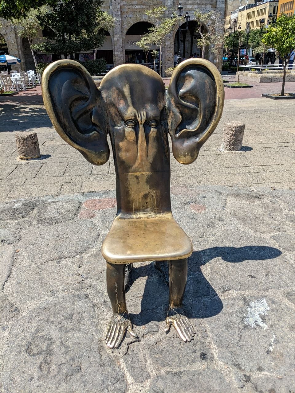 Surrealist bronze chair sculpture with a face and oversized ears on Plaza Guadalajara