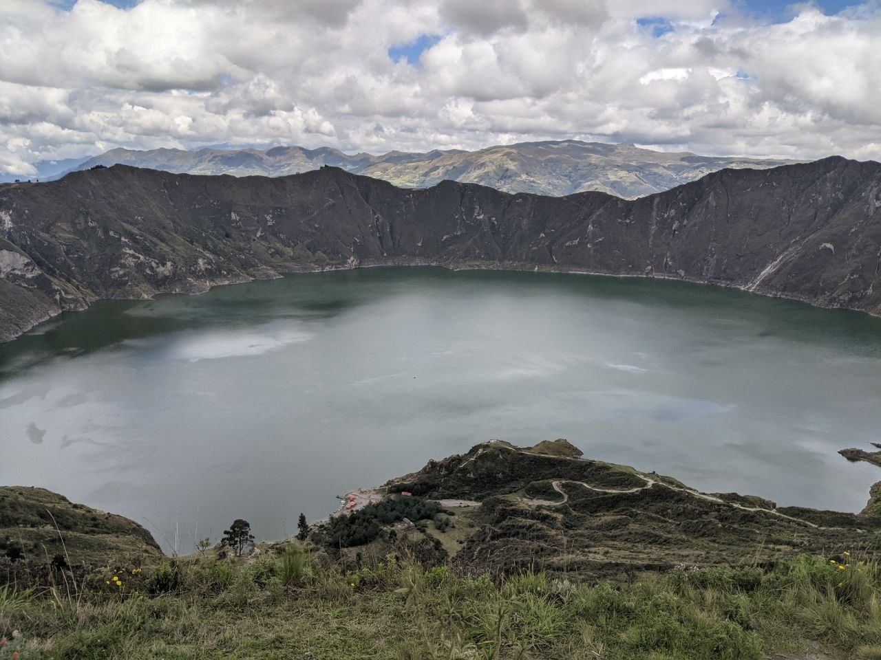 Panoramic view from the Quilotoa crater rim showing the full volcanic lake and small settlement on the shoreline below