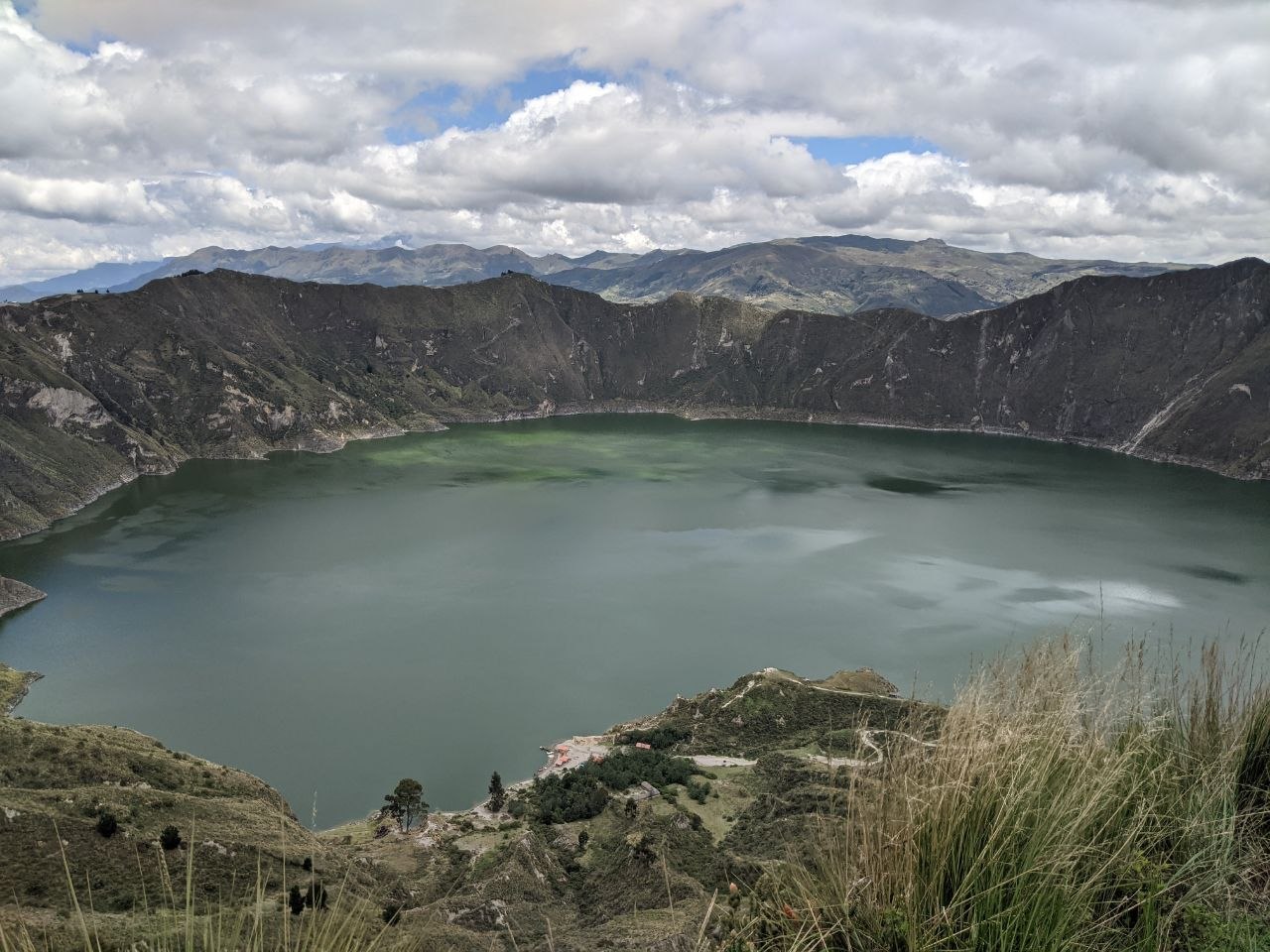 Páramo grasses framing a panoramic view of Laguna Quilotoa from the volcanic crater rim