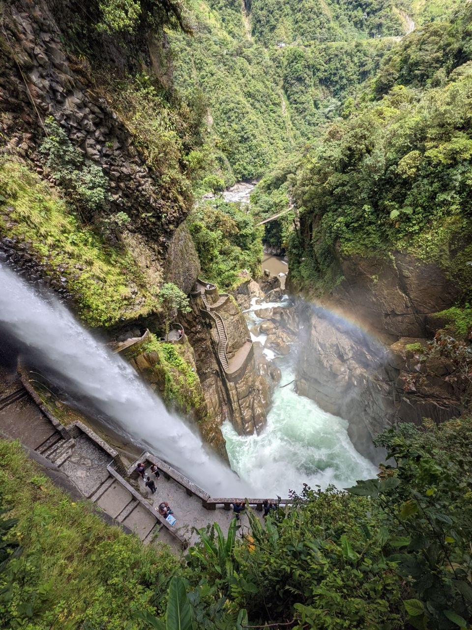Aerial view of Pailón del Diablo waterfall with viewing platforms, spiral staircase, and rainbow over the Pastaza River gorge