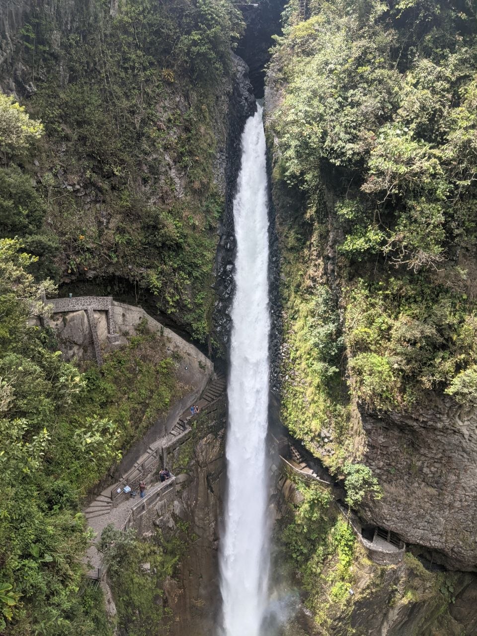 Full-height view of Pailón del Diablo waterfall dropping through a narrow basalt canyon with stepped viewing platforms on both sides