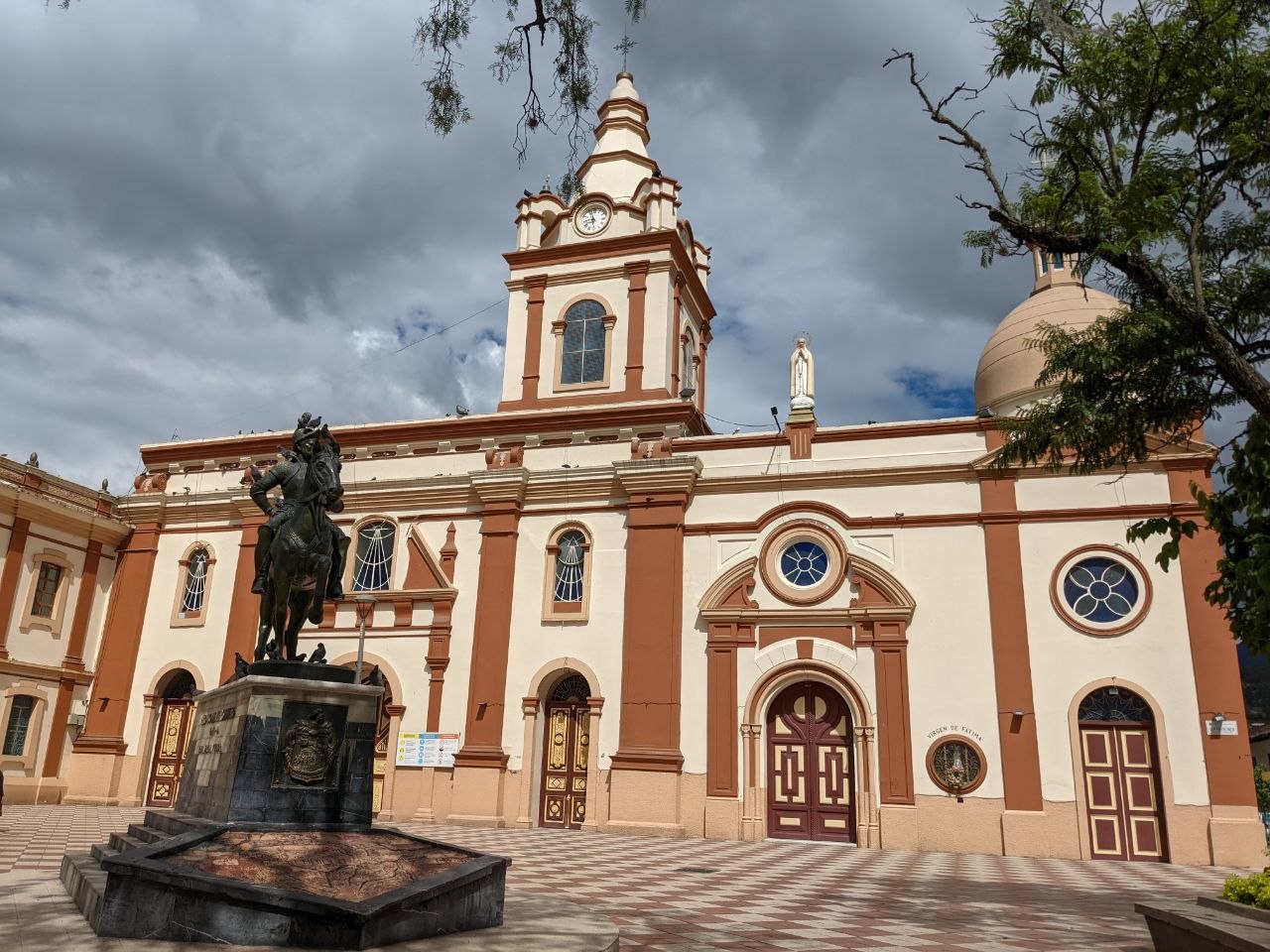 Colonial facade of Loja Cathedral with terracotta and cream detailing, clock tower, and equestrian statue of Bernardo Valdivieso in the foreground