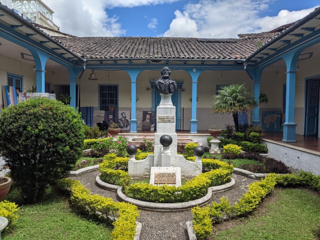 Colonnaded interior courtyard of Colegio Bernardo Valdivieso with blue arched columns, manicured garden, and central bust of Valdivieso
