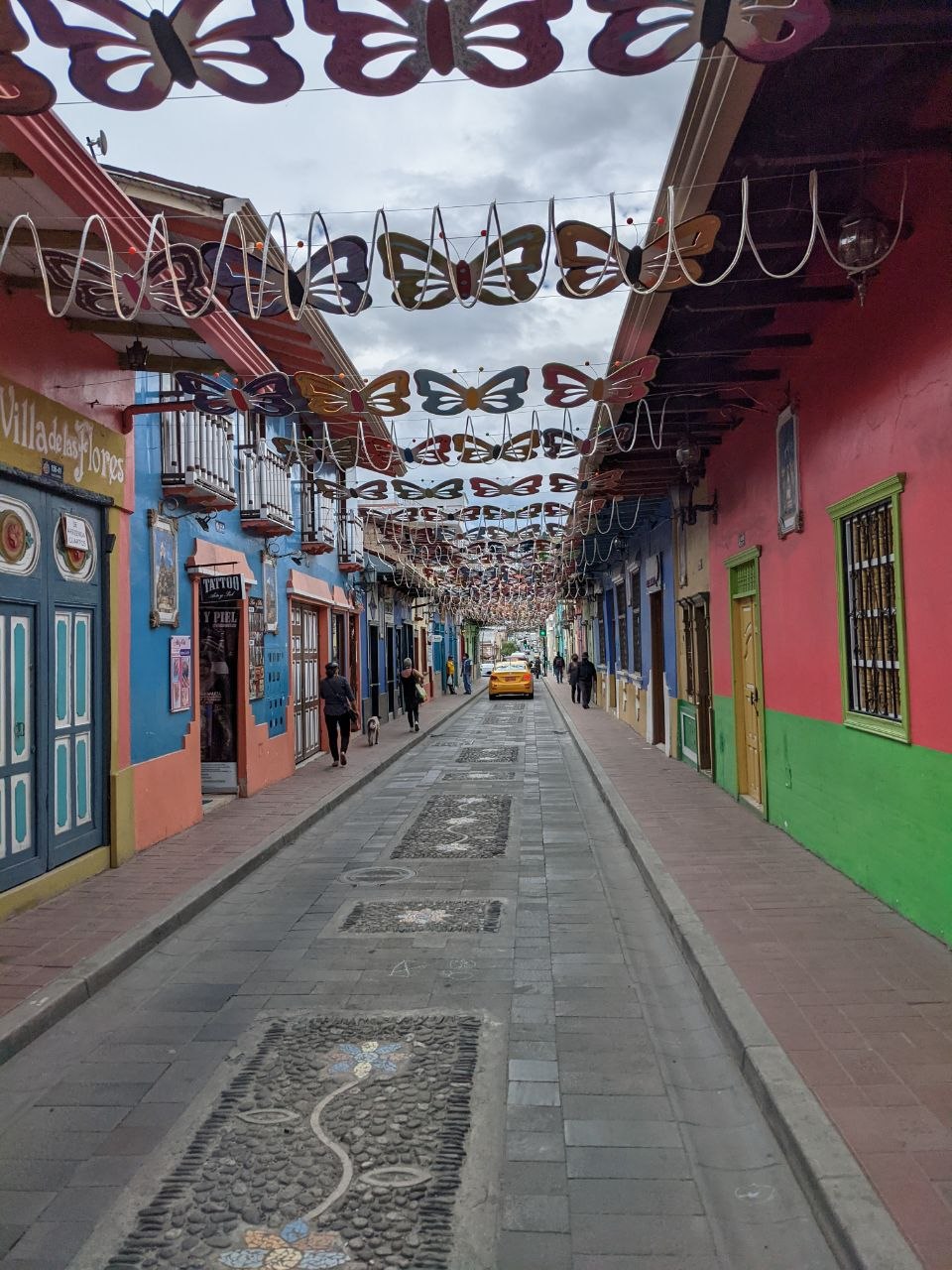 Calle Lourdes pedestrian street in Loja with colourful colonial facades, metal butterfly decorations overhead, and mosaic cobblestone pavement