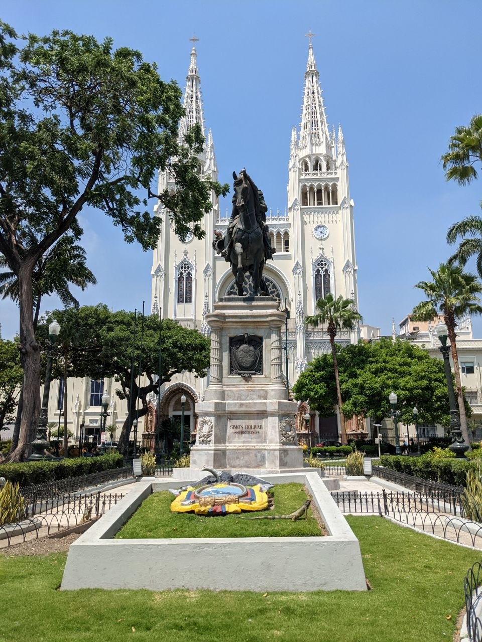 Equestrian statue of Simón Bolívar in Parque Bolívar with the white Neo-Gothic Metropolitan Cathedral of Guayaquil rising behind it under a blue sky