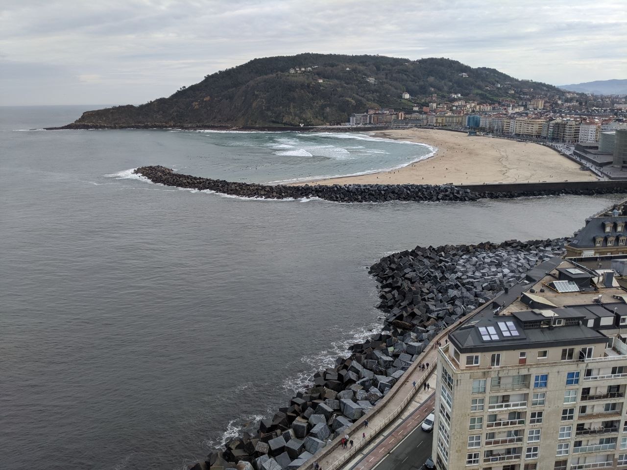 Panoramic view from Monte Igueldo looking over the rocky breakwater, Zurriola beach, and the wooded hill of Monte Urgull across the bay in San Sebastián