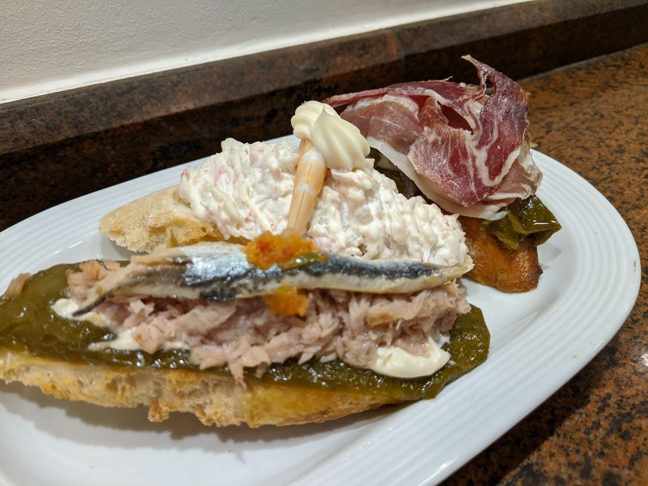 A plate of pintxos in San Sebastián featuring tuna with roasted green pepper and anchovy, and jamón ibérico with pepper on toasted bread