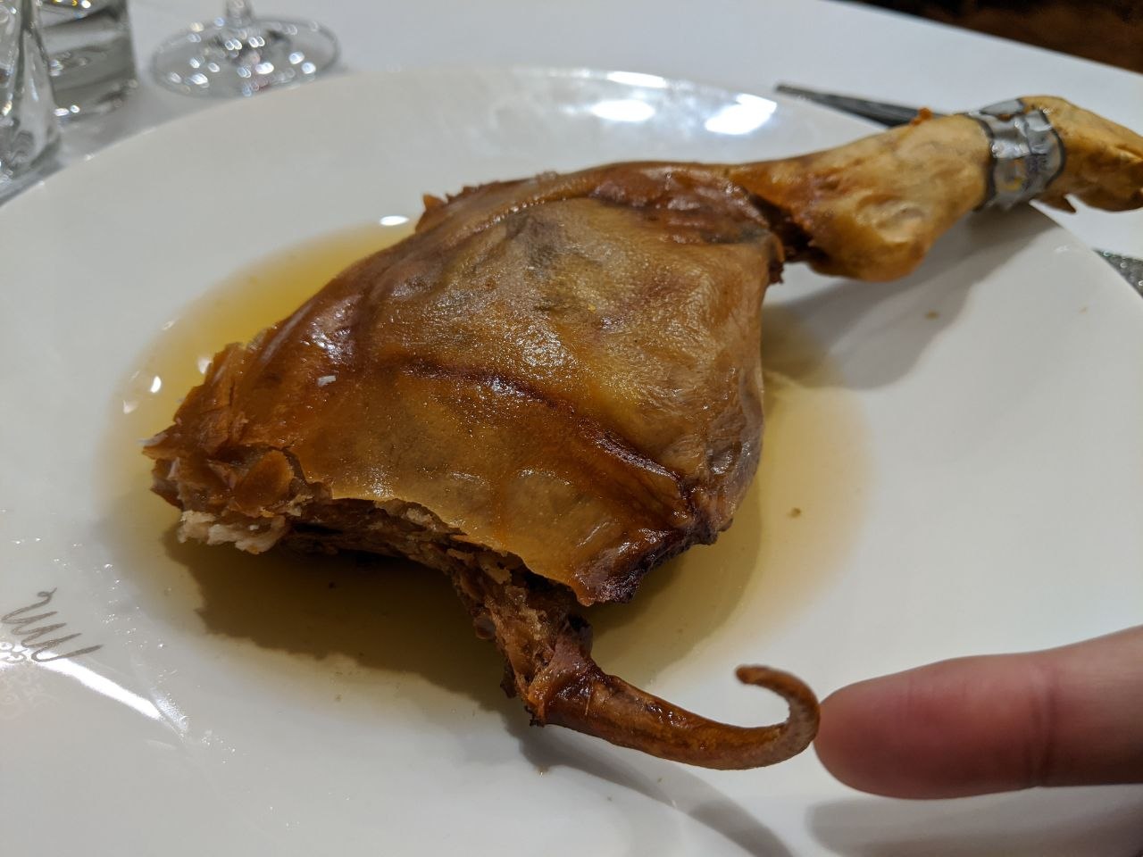 A whole roasted quarter of cochinillo asado — suckling pig with golden crackling skin and a curled trotter — served on a white plate in a Segovia restaurant
