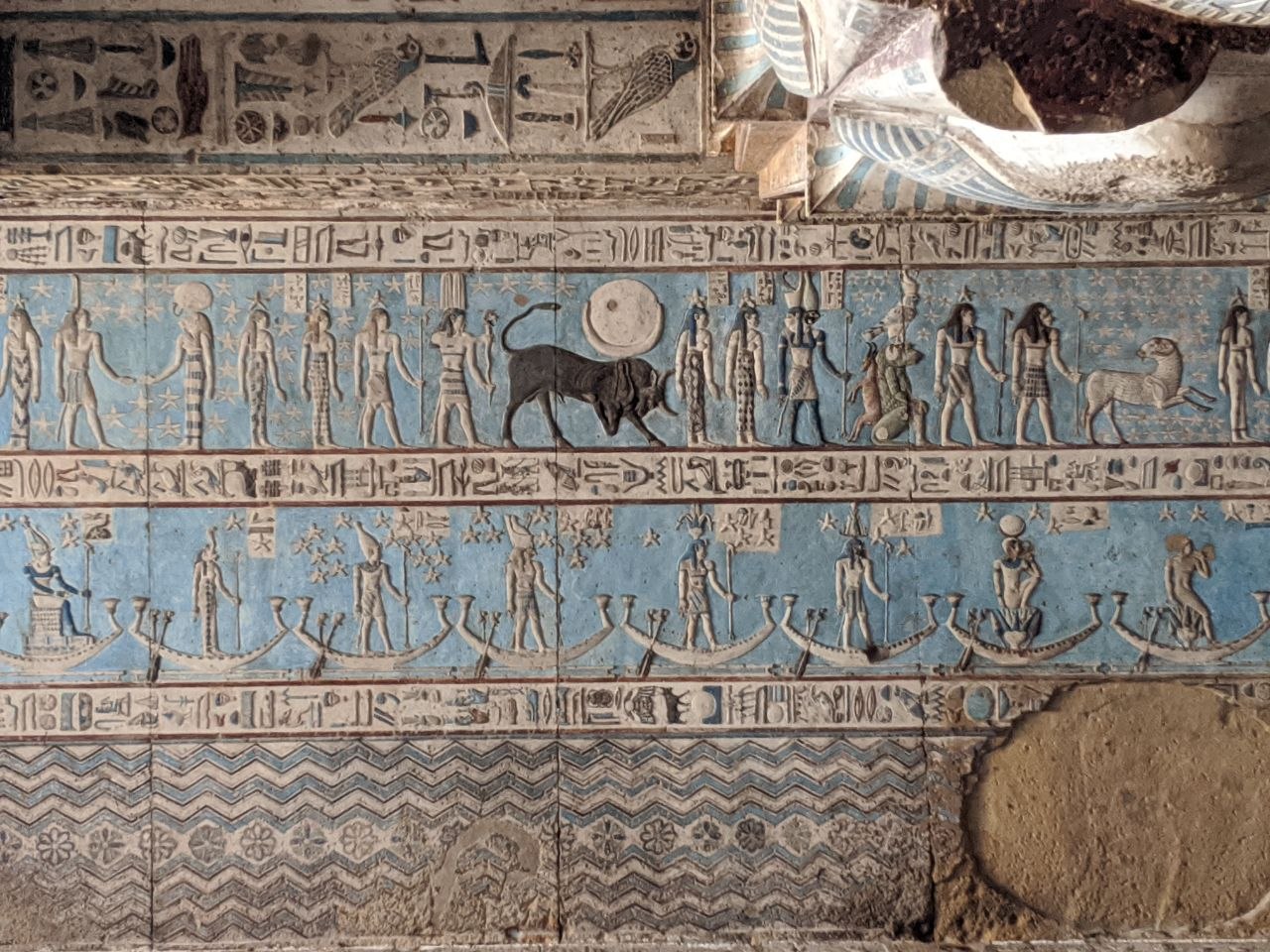 Dendera astronomical ceiling with blue background showing deities, a bull, solar disc, and figures in sacred boats