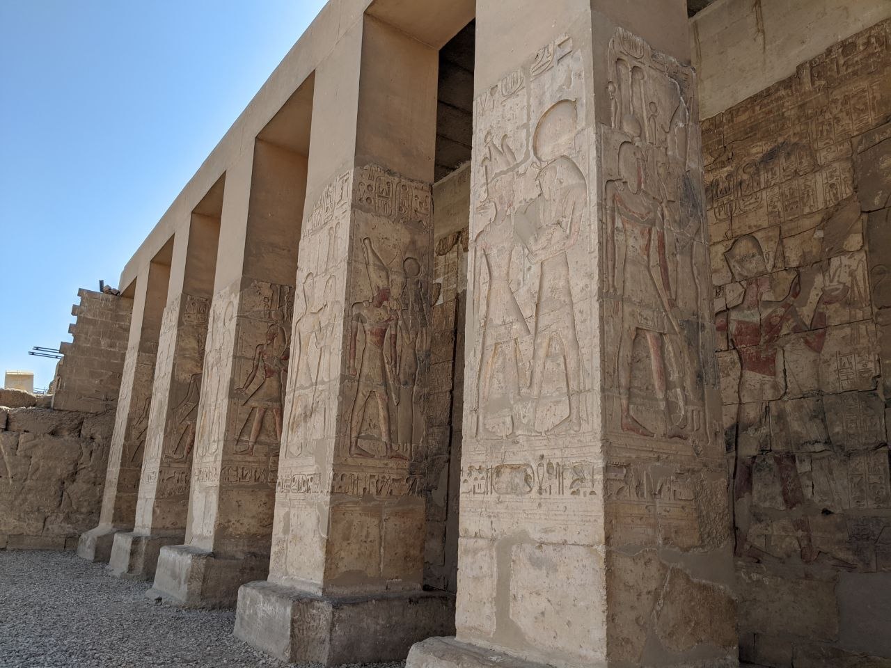 Exterior colonnade of Abydos temple with carved relief figures of pharaohs and gods on the column faces in bright daylight