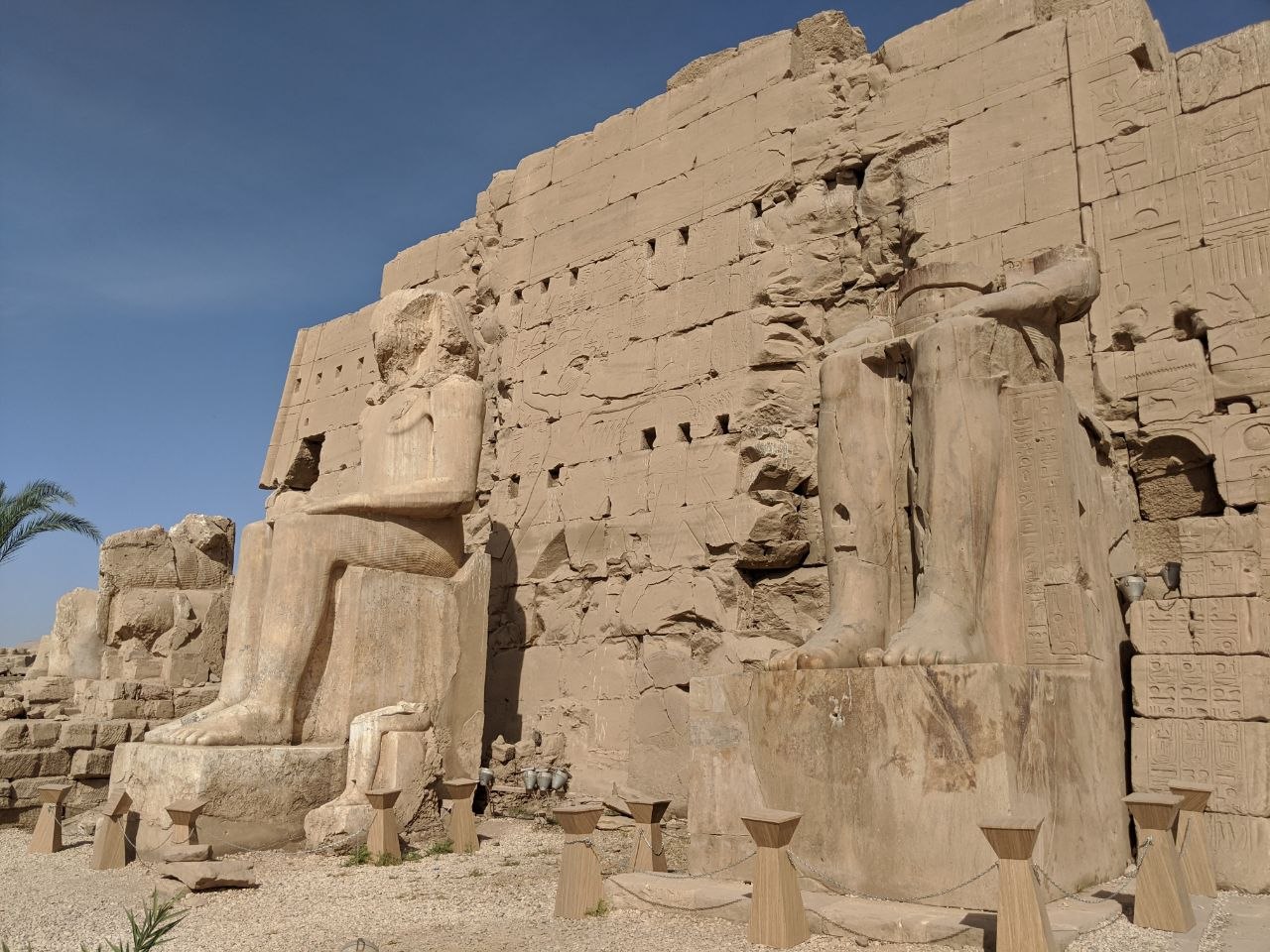 Colossal seated statues of Ramesses II flanking the entrance pylon of Karnak, their upper bodies heavily weathered