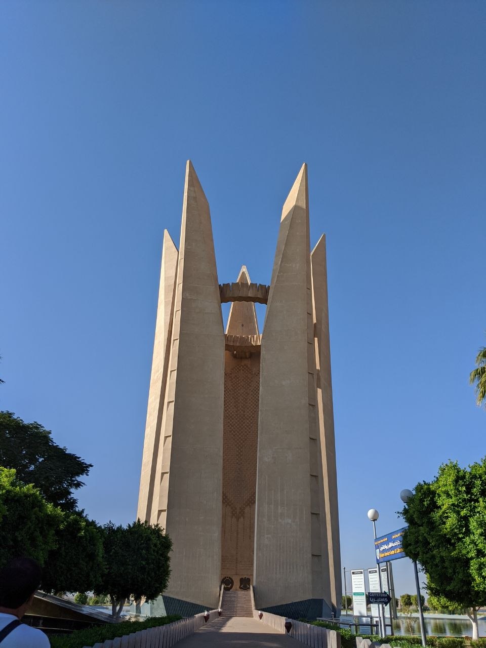 The Soviet-Egyptian Friendship Monument at the Aswan High Dam, four tapering concrete pylons converging toward a central lotus motif against a deep blue sky, flanked by palm trees